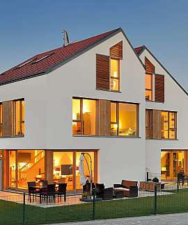 Modernes Einfamilienhaus mit großen Fenstern und beleuchtetem Innenraum in der Abenddämmerung.