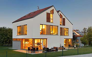 Modernes Einfamilienhaus mit großen Fenstern und beleuchtetem Innenraum bei Dämmerung.