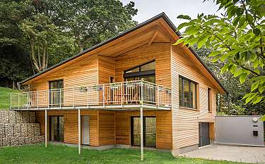 Zweistöckiges Holzhaus mit Balkon und großer Dachschräge inmitten von Bäumen