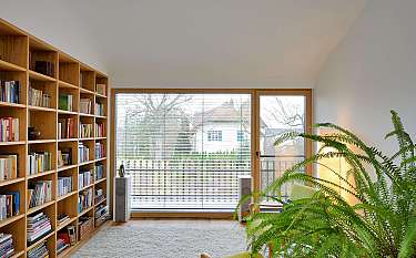 Helles Wohnzimmer mit großem Bücherregal, Fensterfront und grünen Zimmerpflanzen.