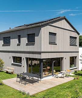 Modernes zweigeschossiges Haus mit Holzterrasse, Garten und ländlicher Umgebung.