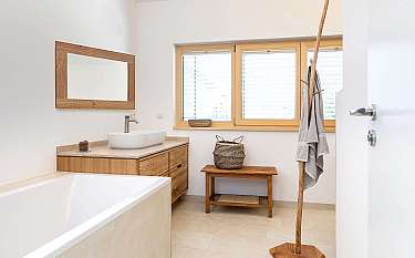 Modernes Badezimmer mit Badewanne, Waschtisch, Spiegel, Fenster und Holzkleiderständer.