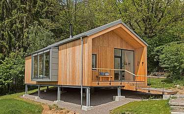 Modernes Holzhaus auf Stelzen mit Terrasse in einer grünen Waldumgebung.