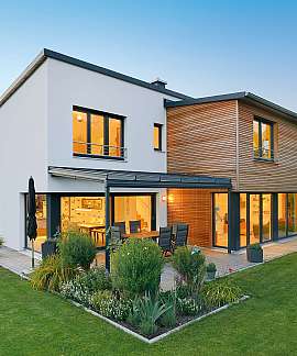 Modernes Haus mit großen Fenstern, Holzverkleidung und gepflegtem Garten bei Tageslicht.