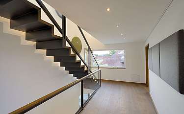 Moderne schwarze Treppe in hellem Flur mit Holzfußboden und großem Fenster.