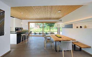 Heller Essbereich mit Holztisch, grauen Stühlen, Kücheninsel und großer Glasfront zum Garten.