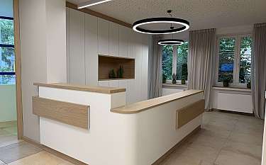 Moderne Empfangstheke in hellem Raum mit runden Deckenleuchten und großen Fenstern.