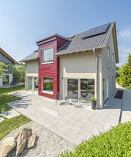Modernes Einfamilienhaus mit rotem Fassadenelement, Terrasse und Garten bei Sonnenschein